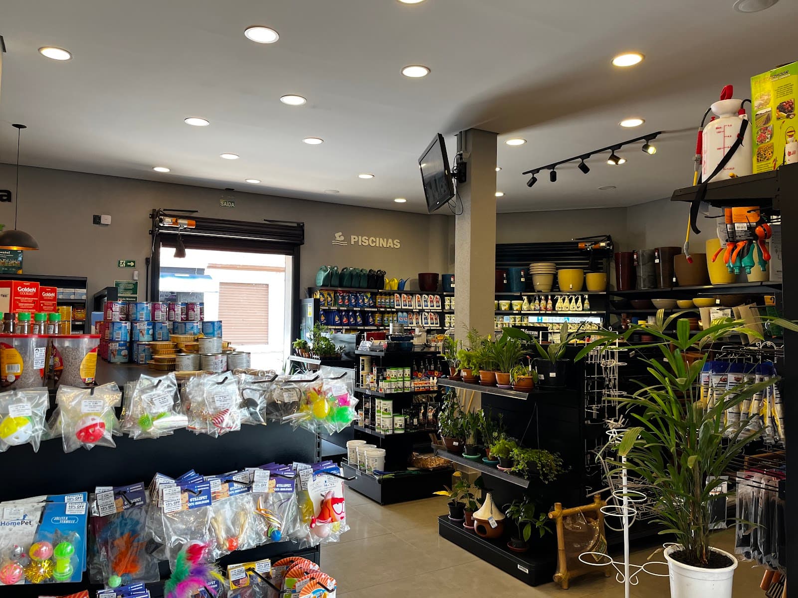 Vista do térreo da loja, com gôndolas de produtos para pet, o corredor de jardinagem e a placa de piscinas ao fundo